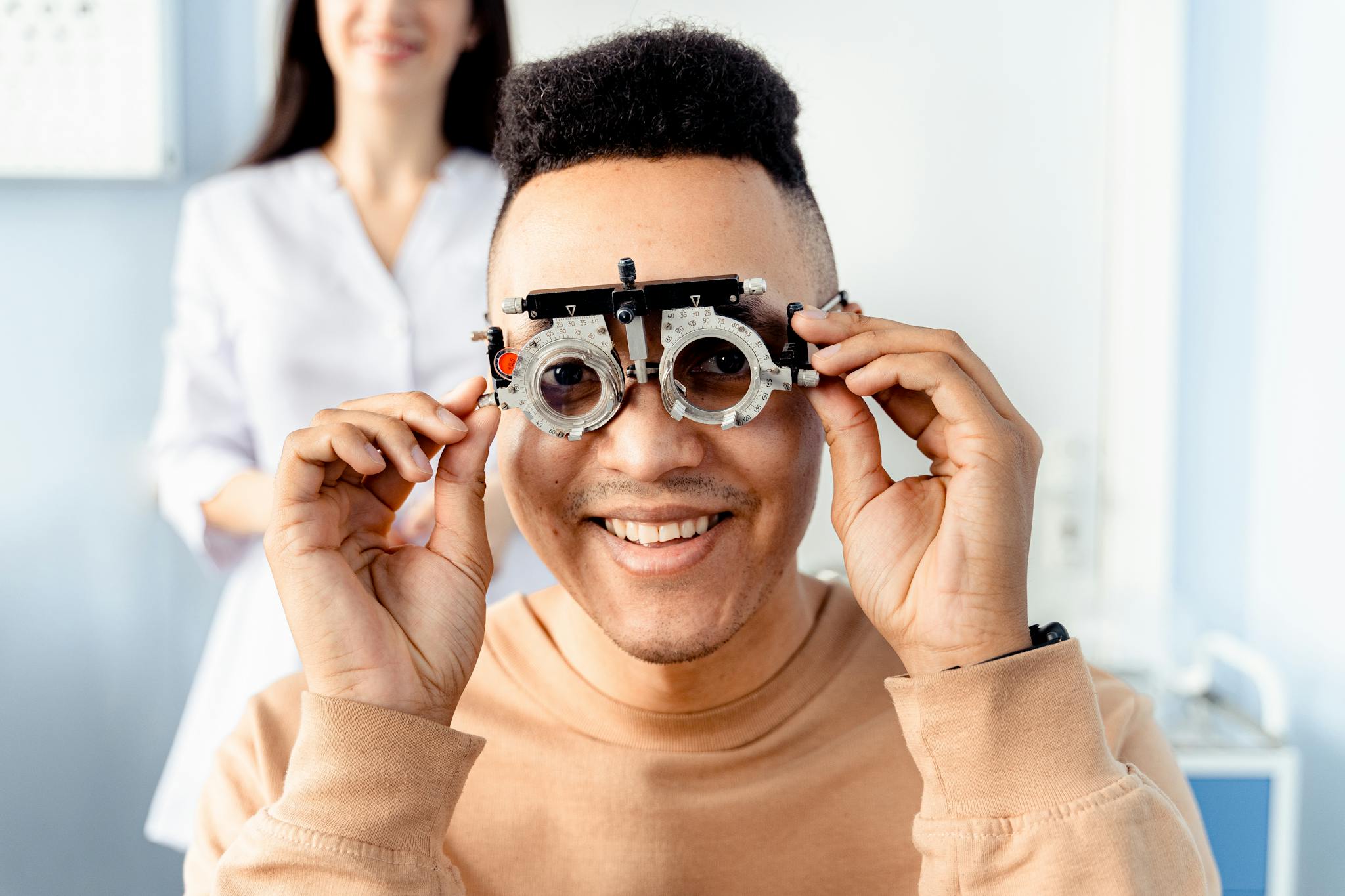 A smiling adult man wearing an optical trial lens frame during an eye exam indoors.