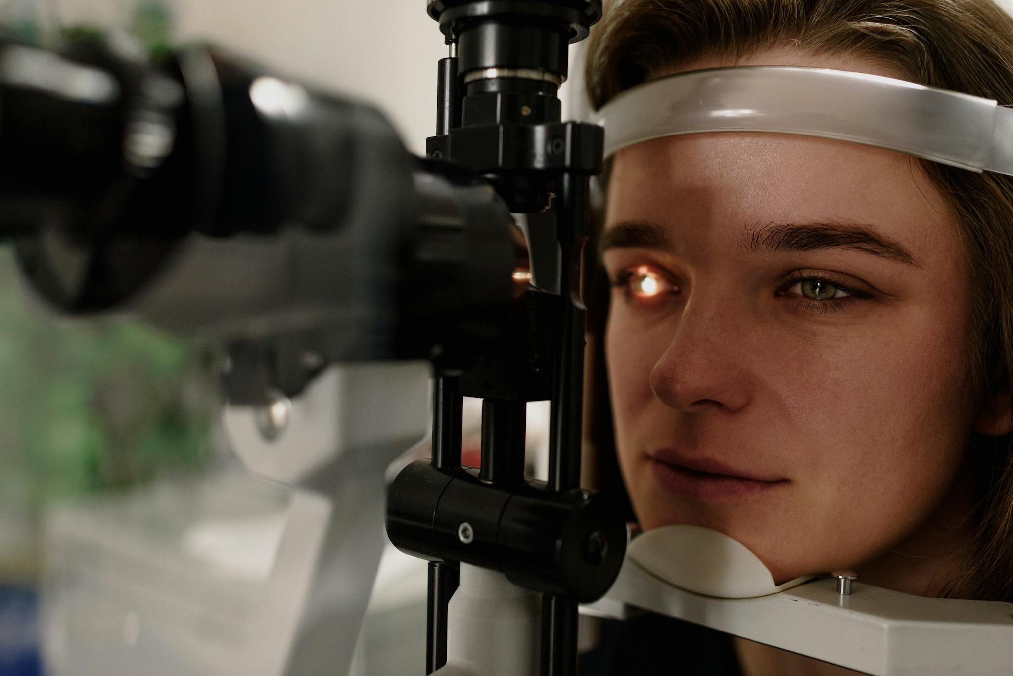 Serious female patient looking at light from contemporary ophthalmic bio microscope while getting eyesight examination in modern clinic during check up